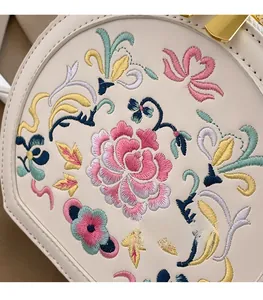 Close-up of exquisite floral embroidery and golden clasp on a cream leather bag