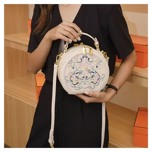 Detail view of floral embroidery on a round crossbody bag with gold metal hardware