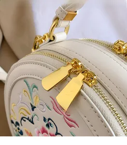 Detailed macro view of high-quality light gold metal zippers on white embroidered round bag