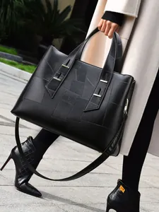 Minimalist black tote bag with geometric texture and gold buckles shown on a model