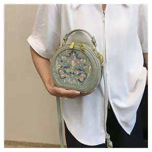 Close-up of vintage flower embroidery on light green round handbag with gold zipper