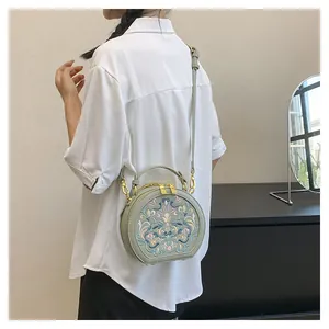 Detail of a round sage green crossbody bag featuring exquisite floral embroidery and gold hardware