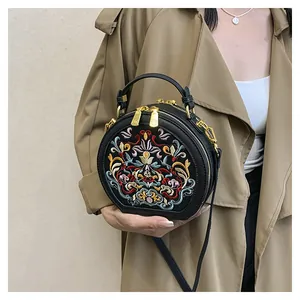 Detail shot of black round bag featuring colorful floral embroidery and gold hardware