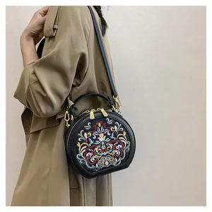 Detail of a black crossbody round bag with colorful ethnic embroidery on a trench coat