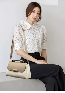 Detail van een minimalistische tweekleurige leren crossbodytas met handvat en zilveren hardware