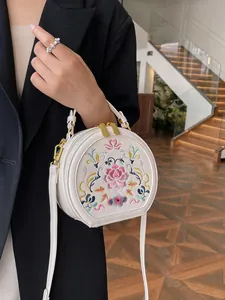 White semi-circle crossbody bag with colorful ethnic embroidery and gold hardware