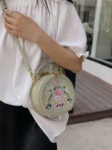 Sage green round crossbody bag with traditional floral embroidery and gold heart zipper