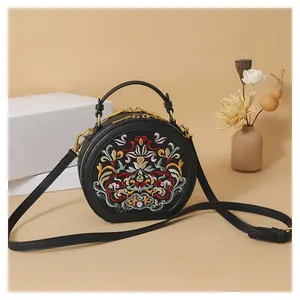 Detailed embroidery on a black round crossbody bag with golden hardware and handles