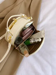 Elegant cream circular crossbody bag with embroidery and gold hardware on a bed