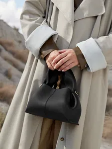 Detail of black lychee grain leather cloud bag styled with a beige trench coat