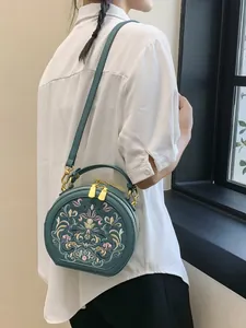 Teal circular crossbody bag with traditional floral embroidery and golden zippers