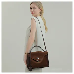 Close-up of a dark brown suede messenger bag with silver twist lock on a minimalist model
