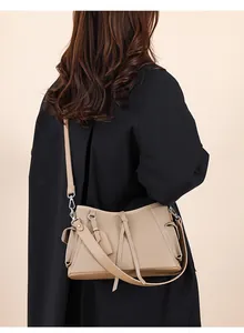 Detailed view of khaki leather shoulder bag with tassel charm on model's back