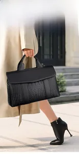 Detail of a black handbag featuring a woven texture and smooth leather flap in a street view