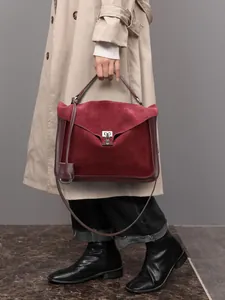 Burgundy faux suede messenger bag with metal buckle held by model in street style