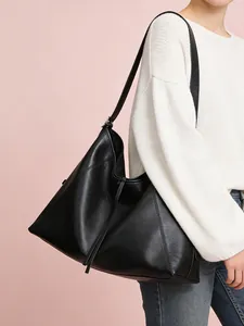 Detalle de bolso tote negro con paneles geométricos y borla sobre un fondo rosa suave