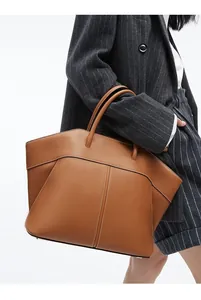 Detail of a large caramel leather tote bag with wing silhouette and twin top handles