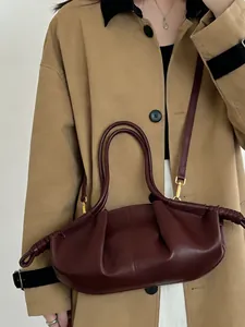 Détail du sac nuage bordeaux avec plis et finitions dorées porté sur un trench-coat