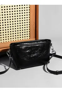 Close-up of black glossy crinkled leather crossbody bag with silver metal hardware
