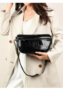 Détail du sac en cuir brillant noir avec texture craquelée et bandoulière tissée