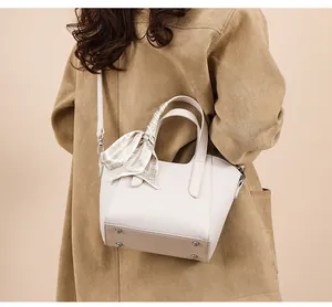 Détail du sac seau en cuir crème avec foulard décoratif et clous de fond en métal