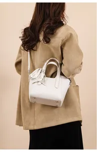 Détail d'un sac seau en cuir crème avec anse en soie porté par un mannequin en beige