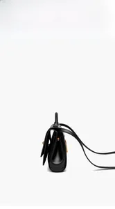Side view of black leather trapezoid handbag with accordion folds and gold hardware