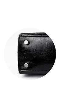 Macro shot of silver metal rivets on the textured black leather base of a crossbody bag
