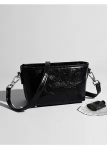 Detail of black cracked leather crossbody bag with silver hardware and glossy texture