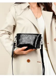 Detail of black cracked texture leather crossbody bag with silver metal feet and strap