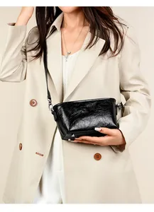 Detail of black cracked leather crossbody bag with shiny texture and silver hardware