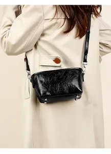 Detailed view of black cracked leather crossbody bag with silver feet on a model