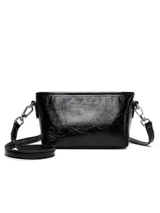 Chic black cracked leather crossbody bag with glossy finish and silver hardware on white back