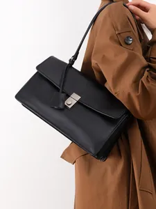 Detail of minimalist black leather shoulder bag with silver metal buckle on a model