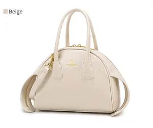 Detail van de beige lederen tas met gouden logo, dubbele handgrepen en metalen beslag