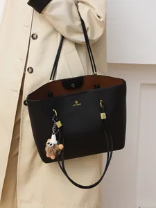 Chic black litchi grain tote bag with brown interior and plush charm on female model