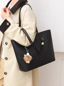 Detail of black pebbled leather tote bag with plush charm on a beige trench coat