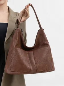 Detail of dark brown hobo bag showing pebbled leather texture and stitching on model