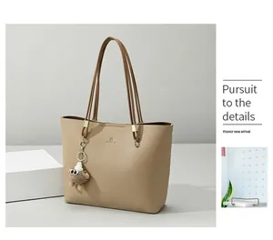 Detail of lychee textured beige tote bag with brown straps and plush monster charm