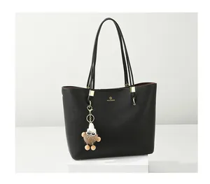 Close-up of black pebbled leather tote bag featuring gold logo and cute plush charm