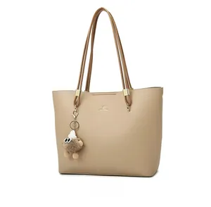 Detail view of beige lychee leather tote bag with gold logo and plush charm