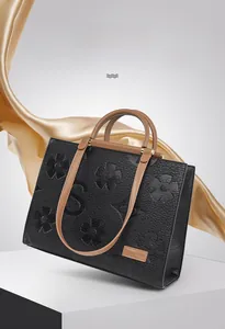 Close-up of black leather tote with embossed floral patterns and khaki contrast handles