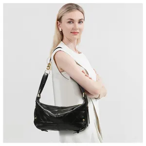 Detail view of black quilted leather shoulder bag with gold hardware on a white outfit