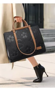 Detail of black leather tote bag with floral embossing and contrasting brown handles