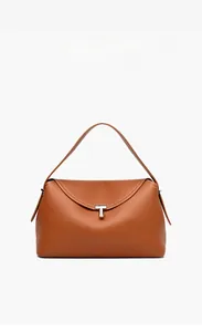 Detail of golden brown lychee grain leather handbag with T-shaped metal clasp and white stitching