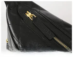 Detail of smooth gold zipper and quilted diamond pattern on black leather shoulder bag