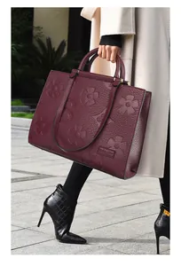 Detail of burgundy leather tote bag featuring 3D floral embossing and metal base feet