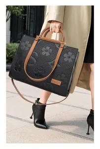 Detail of black embossed tote bag with brown straps and branding on street setting