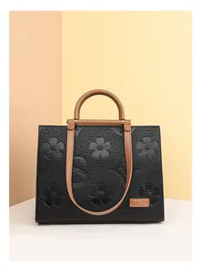 Detailed view of black embossed leather tote with floral patterns and brown brand plaque