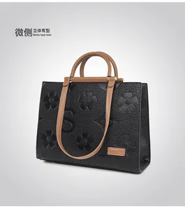 Detail of embossed floral texture and logo patch on black leather tote bag